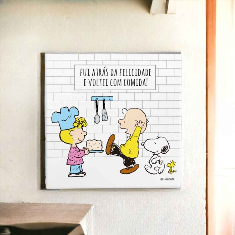 Na foto um azulejo decorativo criativo e engraçado com desenho do Snoopy com um boné e o woodstock em uma cozinha com louças na pia. No azulejo tem a frase enquanto houver vida haverá louça na pia.