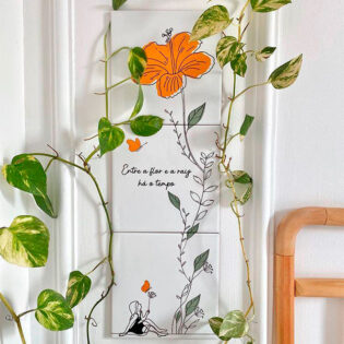 Azulejo decorativo com a frase Entre a flor e a raiz há o tempo com o desenho de uma menina sentada ao lado de uma flor Trio