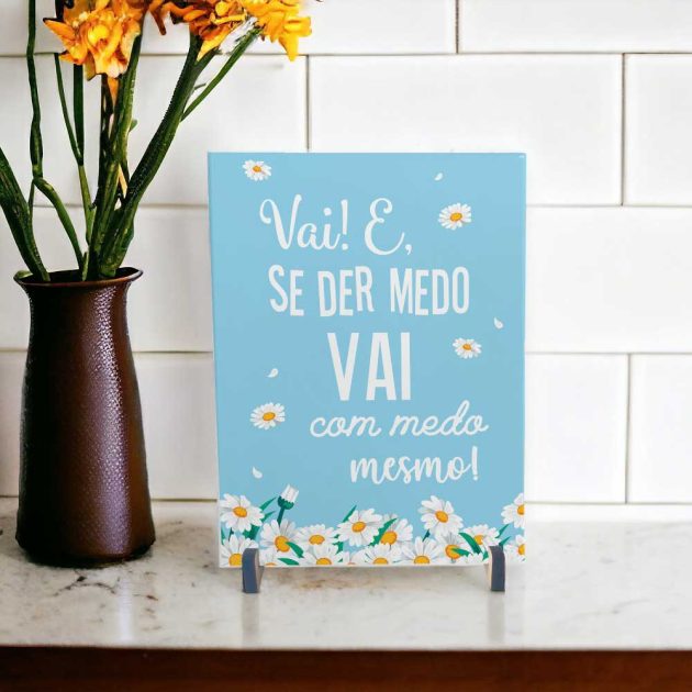 Azulejo decorativo com a frase Vai e se der medo vai com medo mesmo no tom azul com margaridas