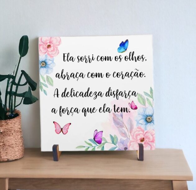 Azulejo decorativo com a frase Ela sorri com os olhos, abraça com o coração. A delicadeza disfarça a força que ela tem